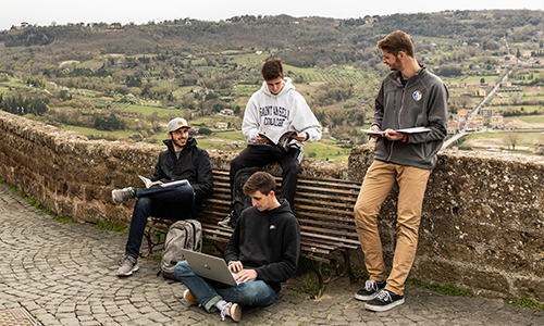 students chat on a wall along the Orvieto landscape