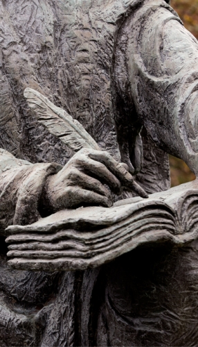 statue of St. Benedict, closeup of hand writing in book