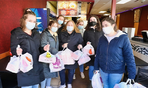 students stand in a restaurant holding bags of food
