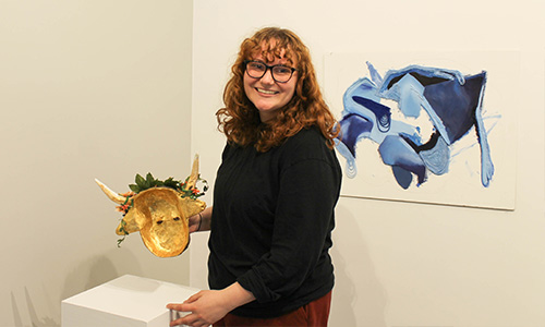 student poses with art pieces in a gallery