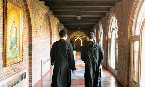 monks walk down a brick hallway