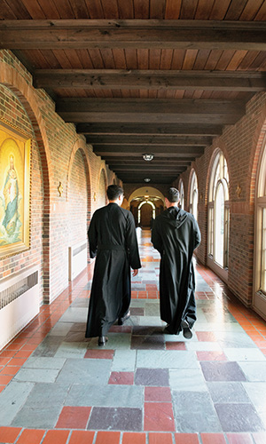 two monks walk down a brick hallways