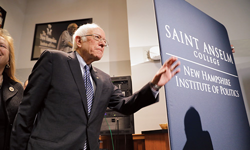 Bernie Sanders stands in front of NHIOP sign