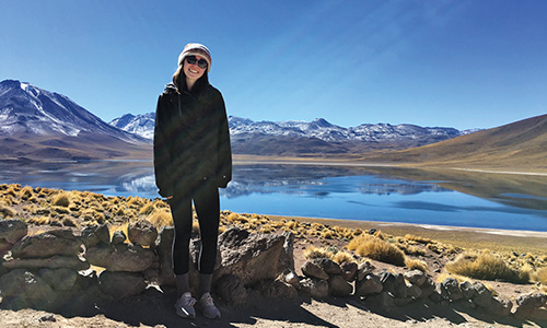 teacher poses in front of a lake with mountains