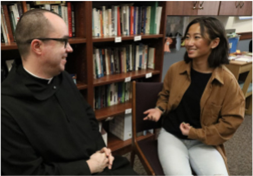 Fr. Lawson with student assistant talking in front of bookshelf