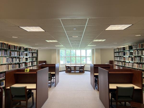 Individual study carrels and large table by a window, between book stacks