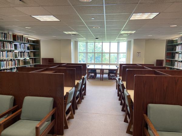Soft chairs, individual study carrles, and large table by window, between book stacks