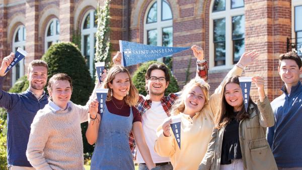 students hold Saint Anselm College pennants in front of alumni hall