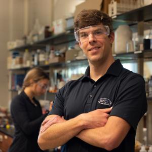 A lab instructor stands in the lab as students work on experiments behind him