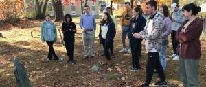 Students stand around a gravestone in Goffstown