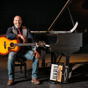 Joe Deleault sits on stage with a guitar in his lap