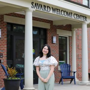 Jill Dorazio '24 standing and smiling in front of the Savard Welcome Center