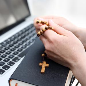 Person praying the rosary in front of a laptop