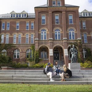 Students sitting on stairs in front of a building on a college campus
