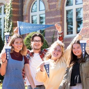 students hold Saint Anselm College pennants in front of alumni hall