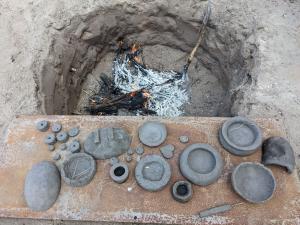 A selection of clay bowls and objects sitting in a pit ready for firing.