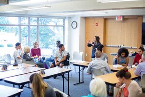 Woman stands in a room speaking to a group of diverse attendees