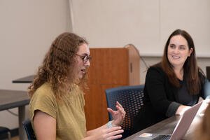 Female student speaks while looking at a laptop while female professor looks on