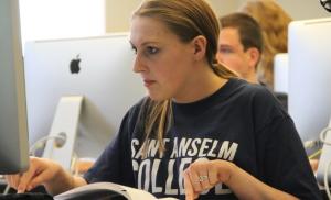 Student looking at computer while pointing to reference sheet