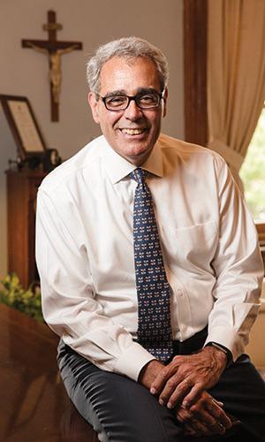 President Favazza sitting on his desk, smiling at the camera