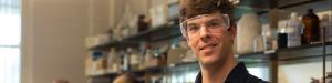 A lab instructor stands in the lab as students work on experiments behind him