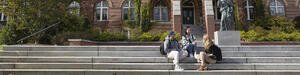Students sitting on stairs in front of a building on a college campus