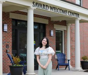 Jill Dorazio '24 standing and smiling in front of the Savard Welcome Center
