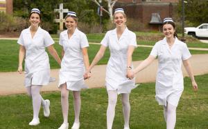 Nurses in pinning ceremony uniforms, holding hands while walking on Alumni Quad