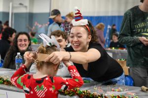 Student places a paper reindeer hat on a child at the fair
