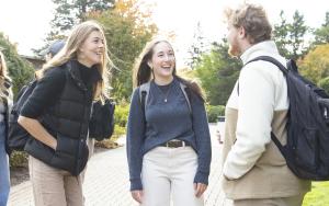 Three students laughing and talking outside on a college campus.